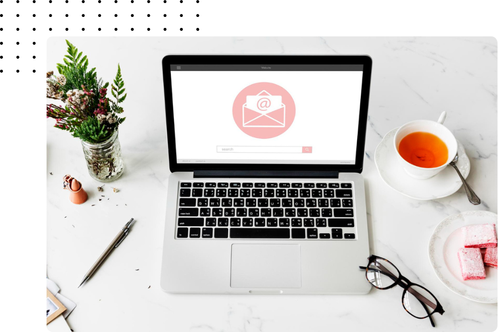 Workspace with a laptop displaying an email icon, a tea cup, glasses, and a plant.